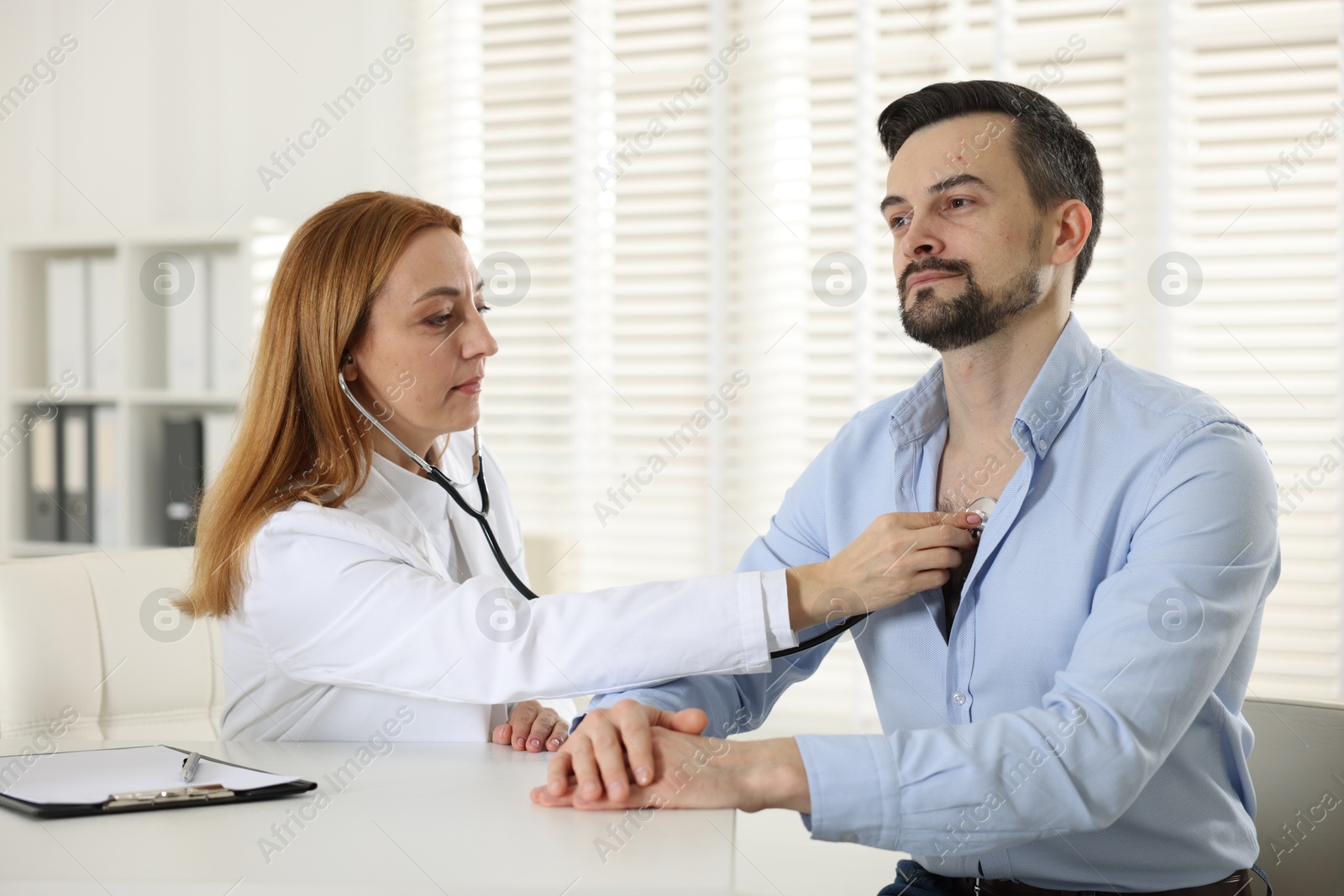 Photo of Cardiologist with stethoscope listening patient's heartbeat at desk in hospital