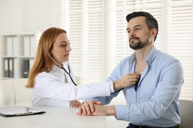 Photo of Cardiologist with stethoscope listening patient's heartbeat at desk in hospital