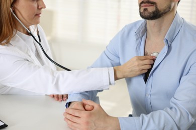 Photo of Cardiologist with stethoscope listening patient's heartbeat at desk in clinic, closeup