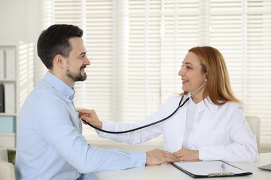 Photo of Cardiologist with stethoscope listening patient's heartbeat at desk in hospital