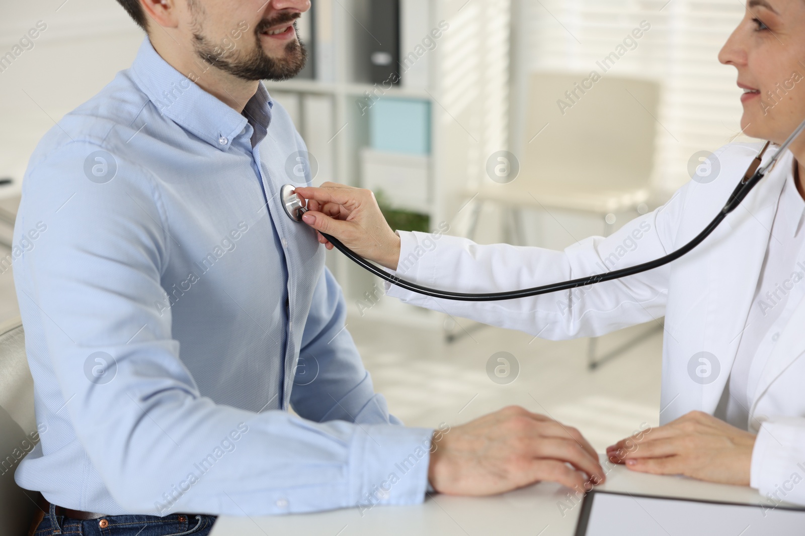 Photo of Cardiologist with stethoscope listening patient's heartbeat at desk in clinic, closeup