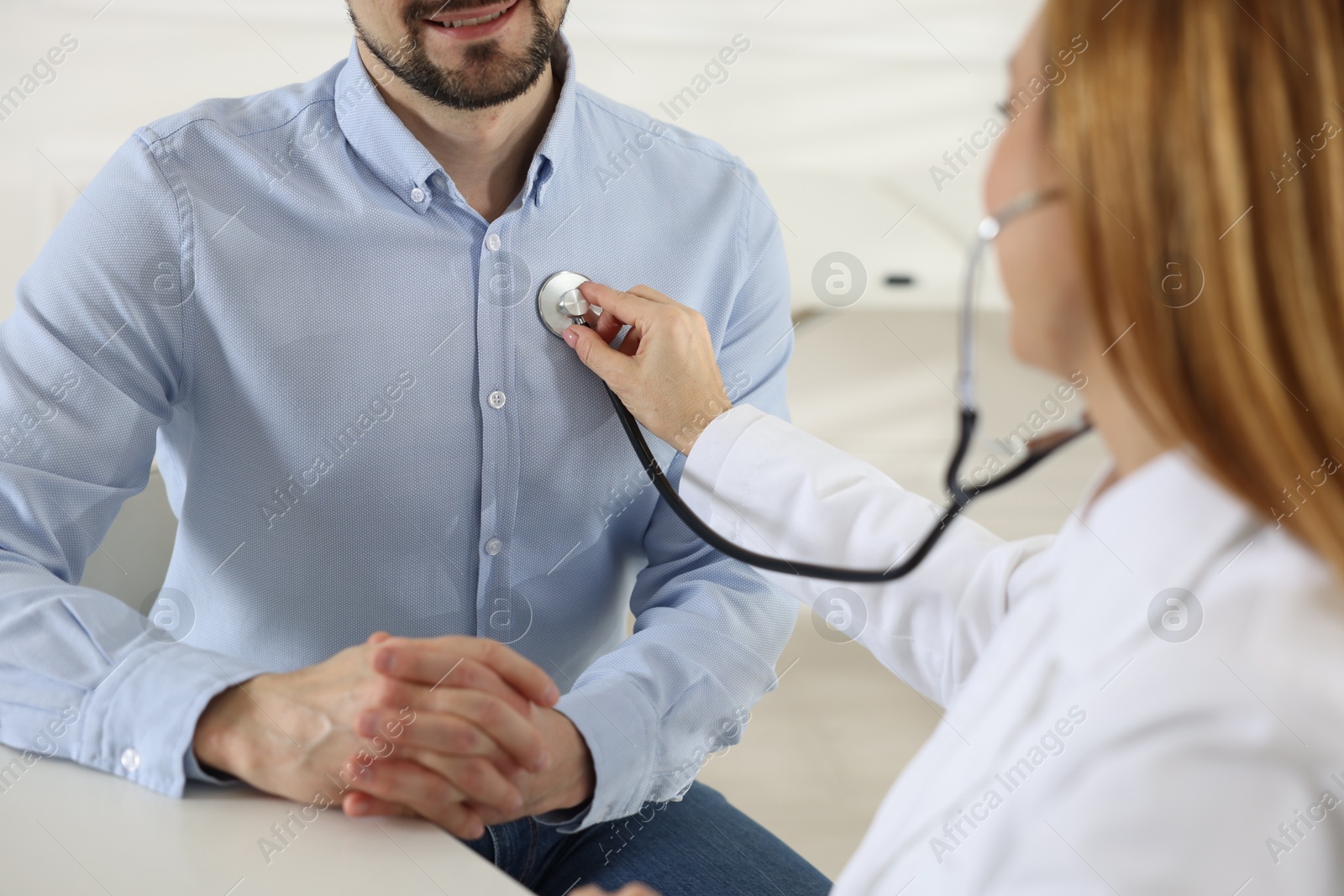 Photo of Cardiologist with stethoscope listening patient's heartbeat at desk in clinic, closeup