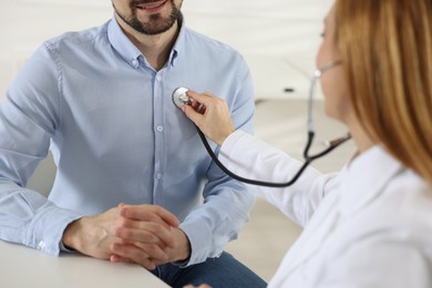 Photo of Cardiologist with stethoscope listening patient's heartbeat at desk in clinic, closeup