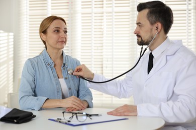 Photo of Cardiologist with stethoscope listening patient's heartbeat at desk in clinic