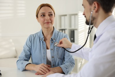 Photo of Cardiologist with stethoscope listening patient's heartbeat at desk in clinic