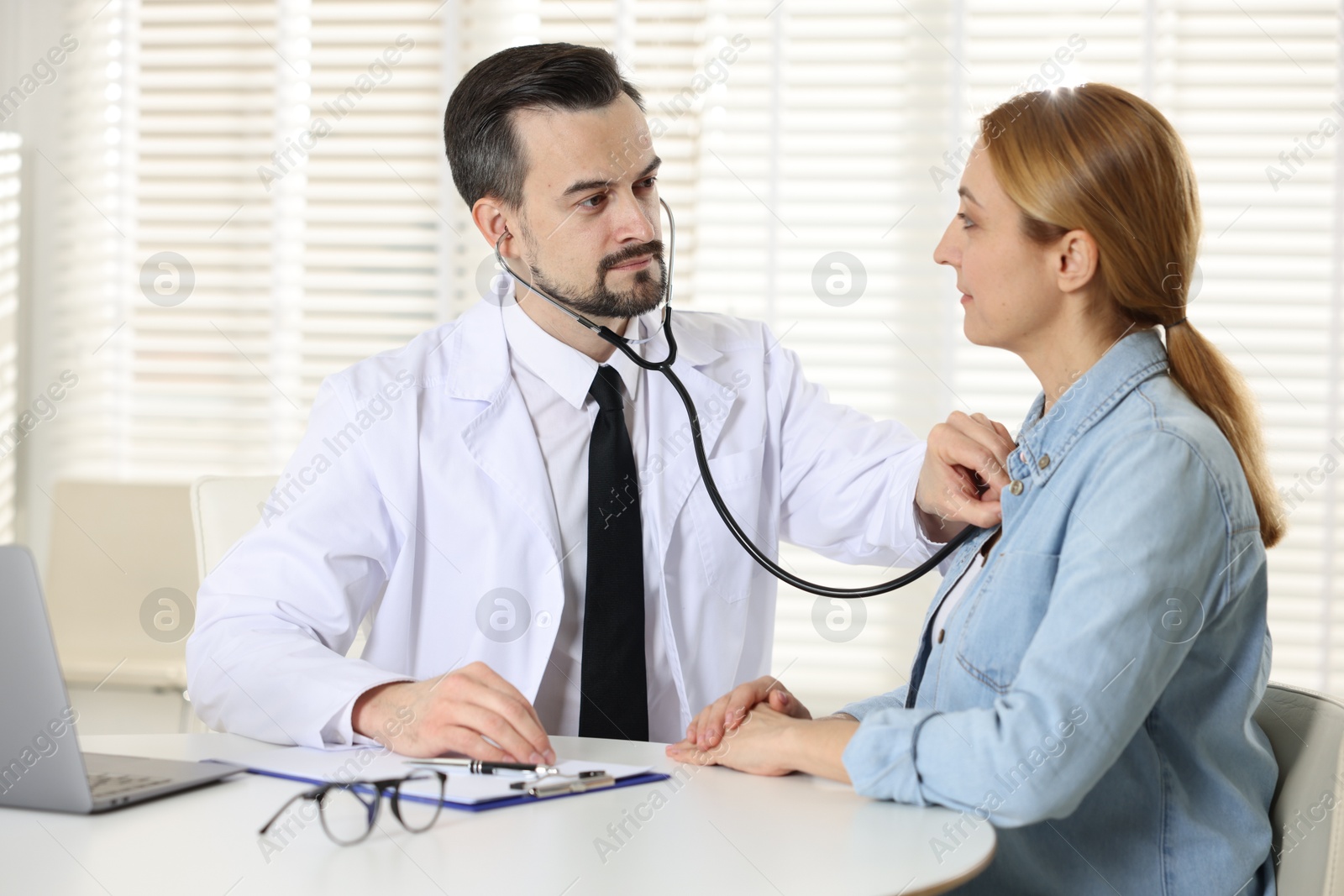 Photo of Cardiologist with stethoscope listening patient's heartbeat at desk in clinic