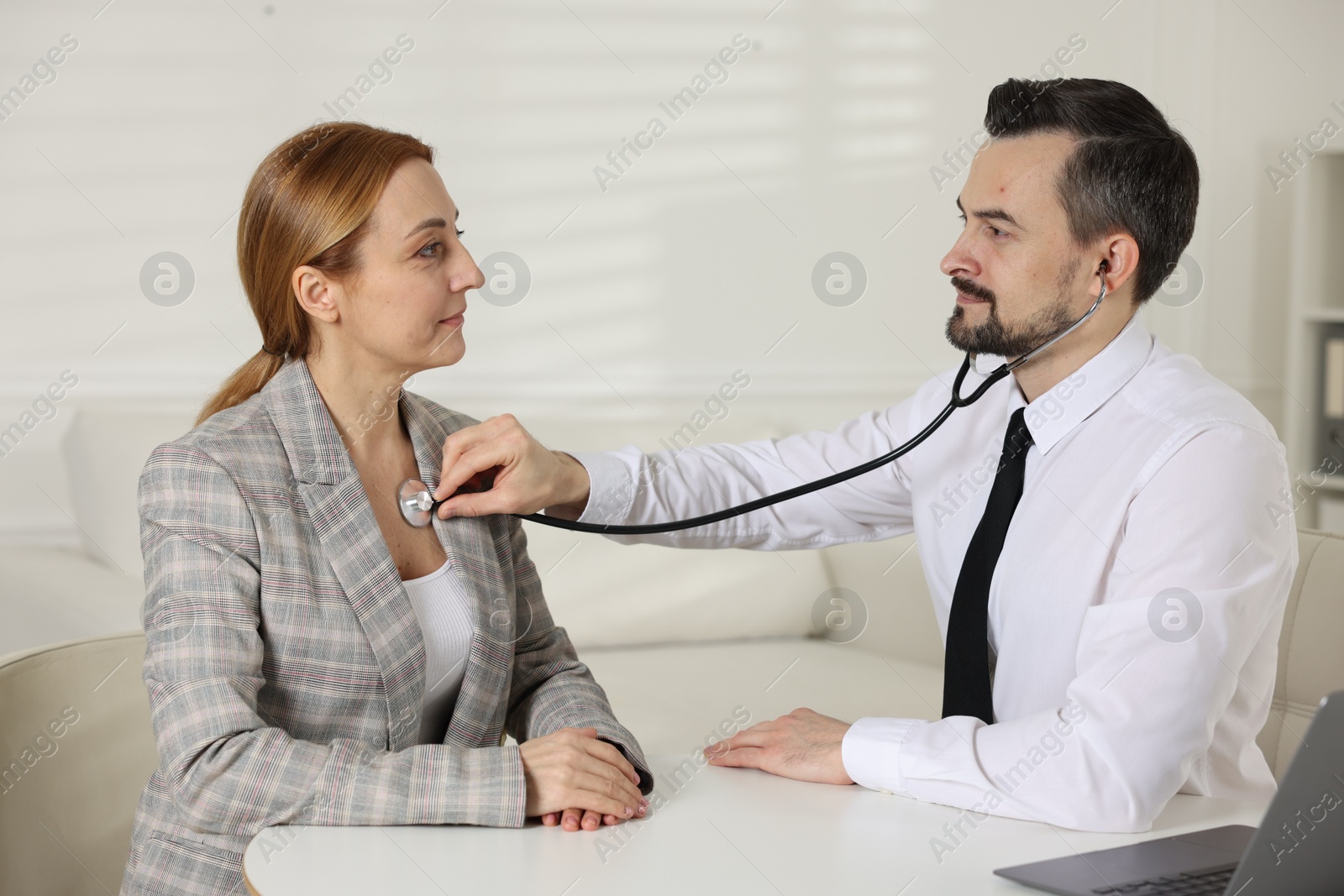 Photo of Cardiologist with stethoscope listening patient's heartbeat at desk in clinic