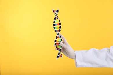 Photo of Scientist holding DNA structure model on yellow background, closeup