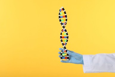 Photo of Scientist holding DNA structure model on yellow background, closeup. Space for text