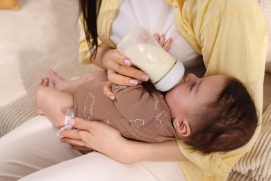 Photo of Mother feeding her little baby from bottle indoors, closeup