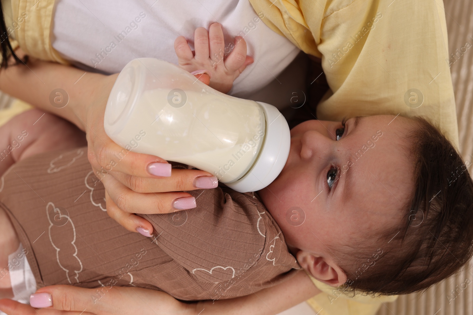 Photo of Mother feeding her little baby from bottle indoors, closeup