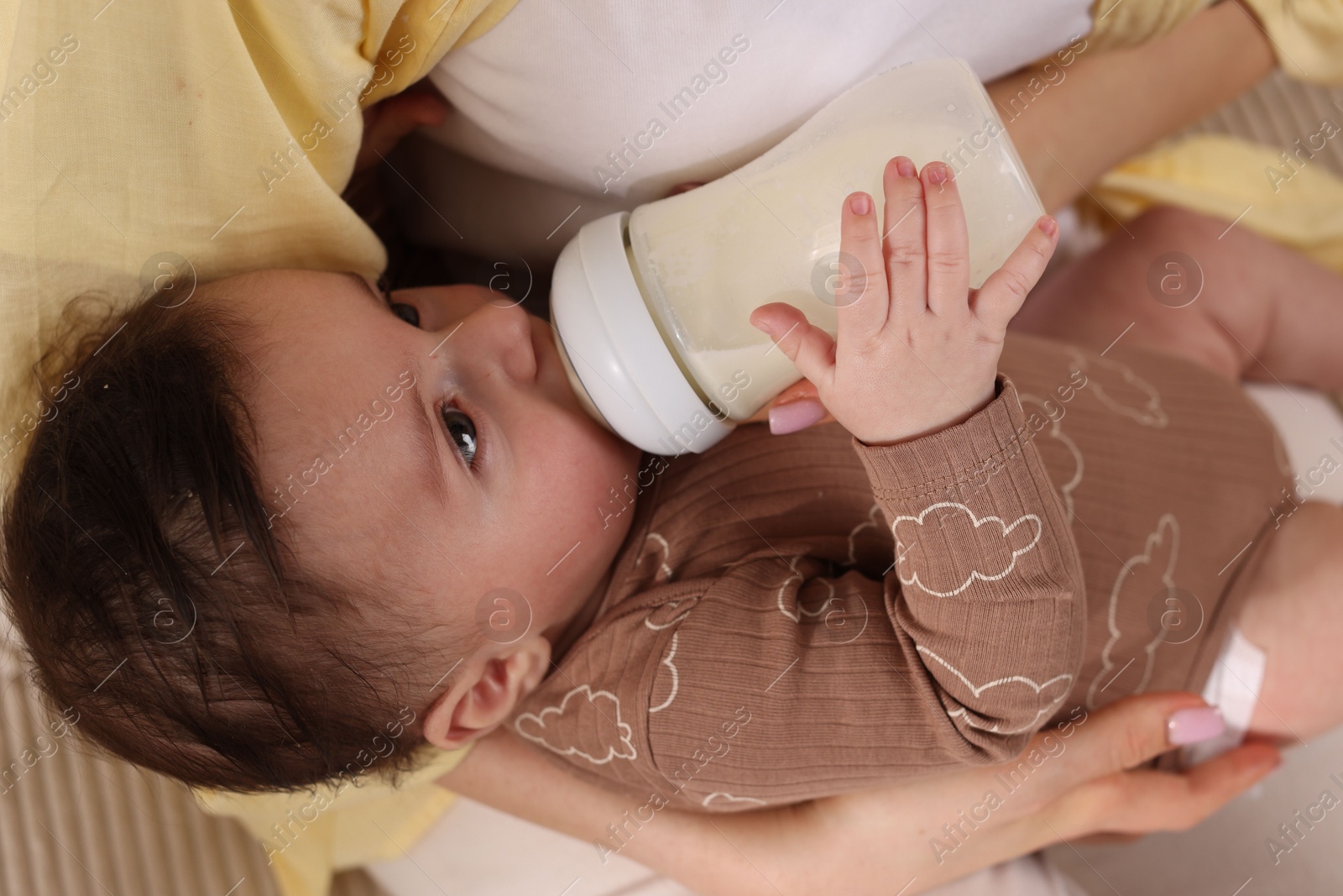 Photo of Mother feeding her little baby from bottle indoors, closeup