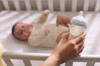 Photo of Mother with feeding bottle of milk near her little baby indoors, selective focus