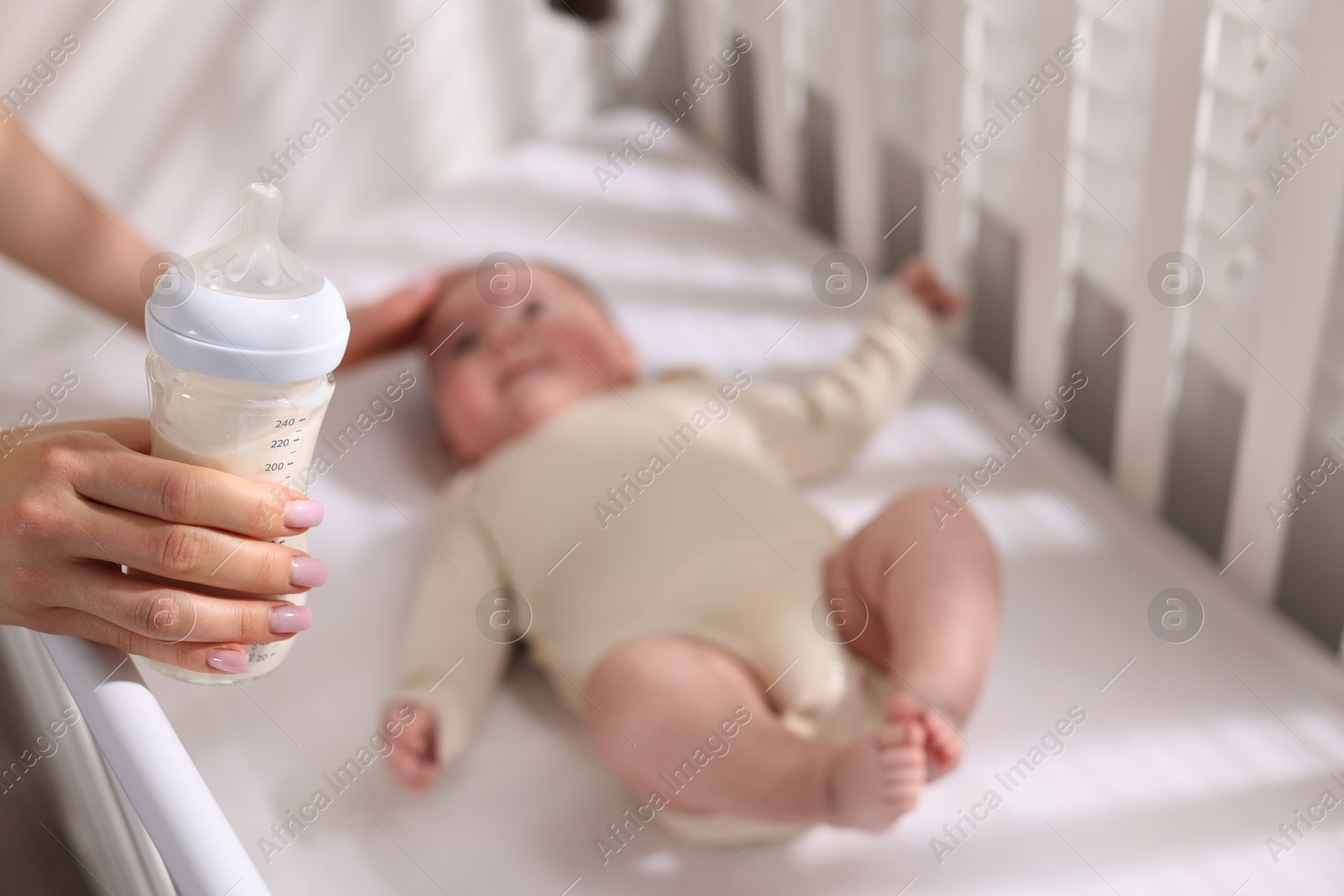 Photo of Mother with feeding bottle of milk near her little baby indoors, selective focus