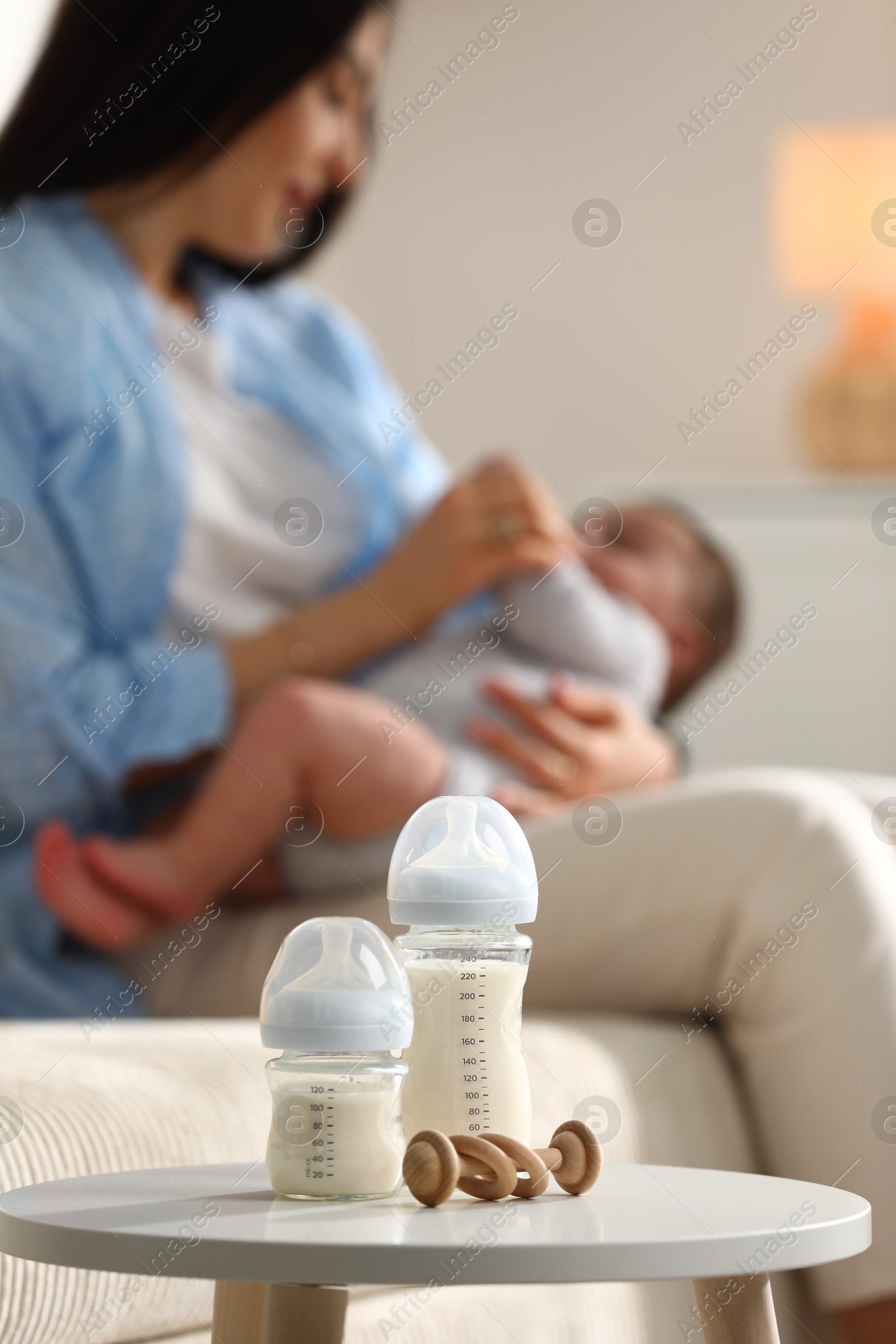 Photo of Mother holding her little baby indoors, focus on feeding bottles with milk and teether