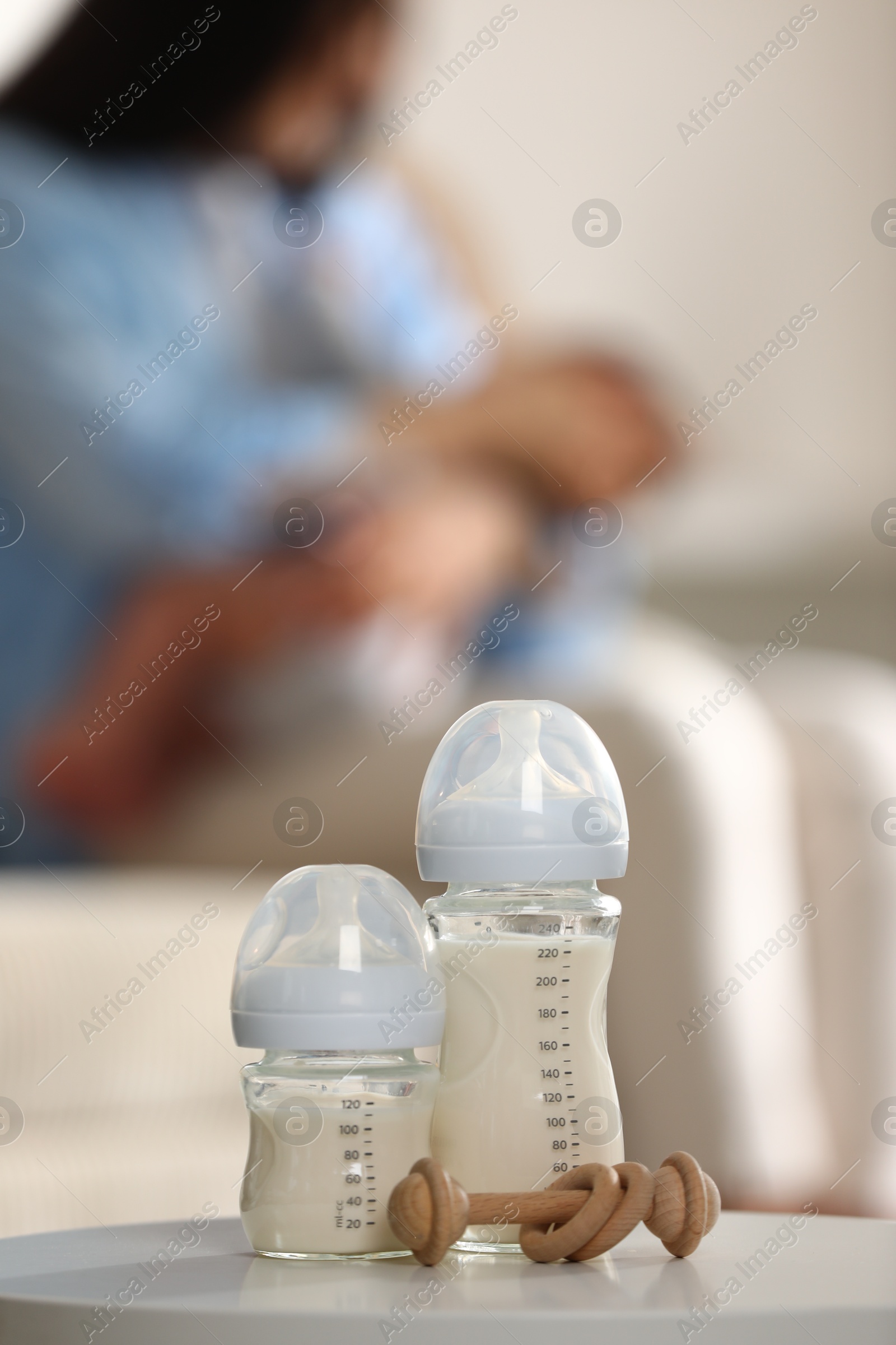 Photo of Mother holding her little baby indoors, focus on feeding bottles with milk and teether