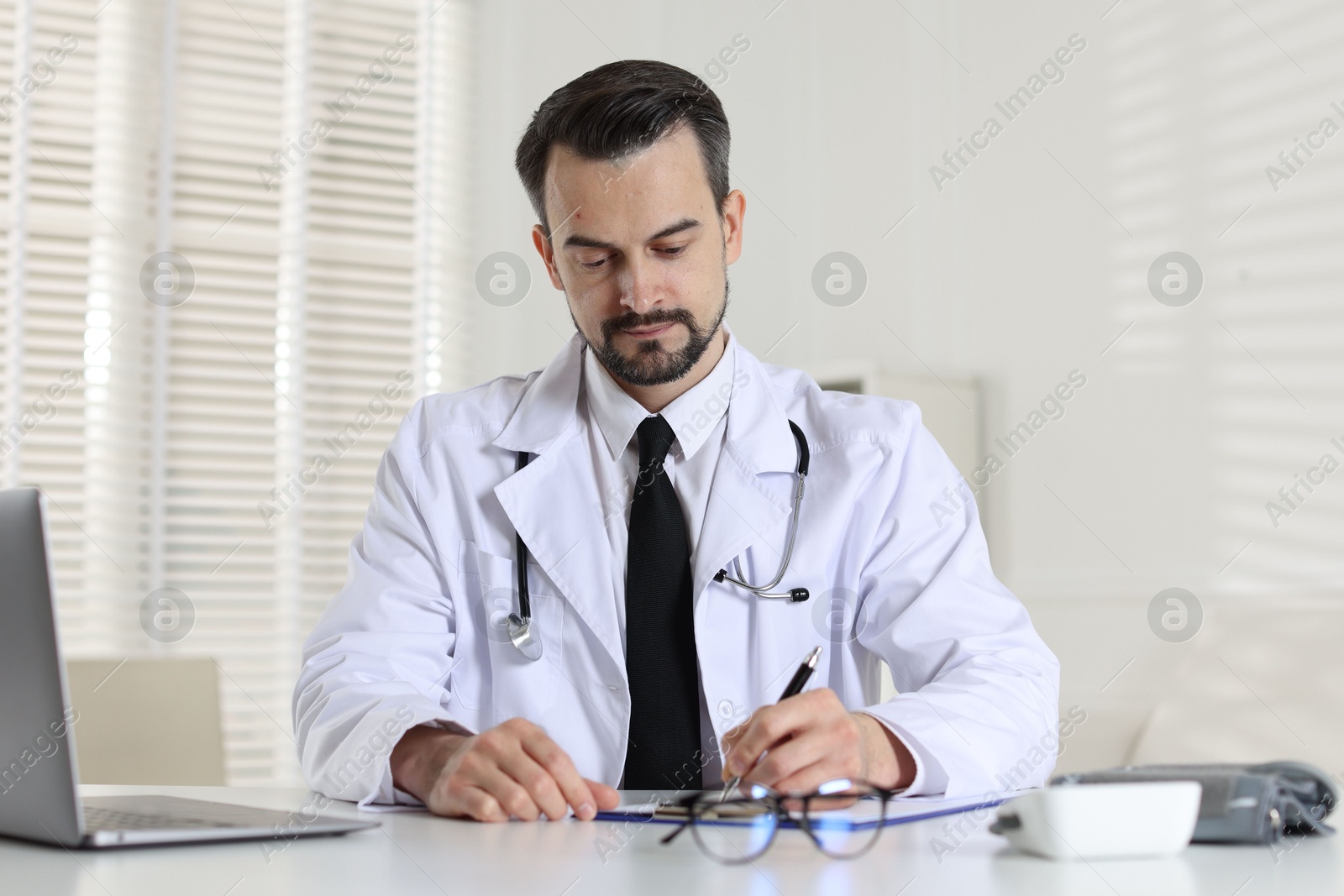 Photo of Cardiologist with stethoscope working at white table in clinic