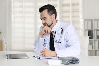 Photo of Cardiologist with stethoscope working at white table in clinic