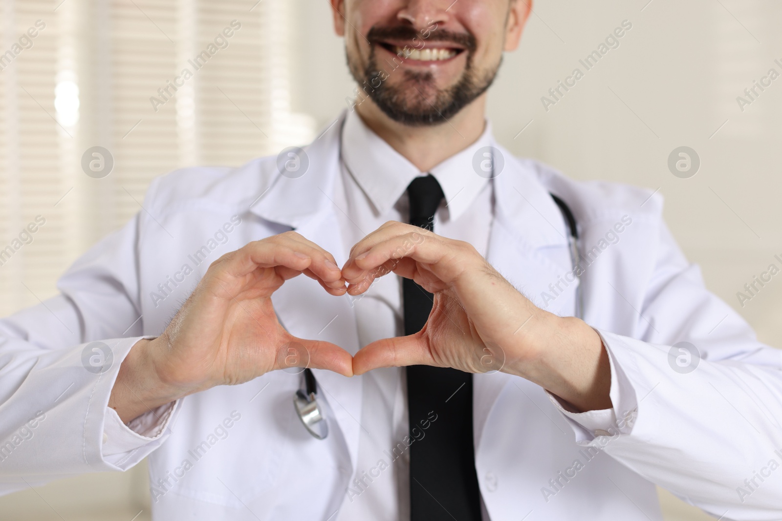 Photo of Smiling cardiologist making heart with hands indoors, closeup