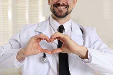 Photo of Smiling cardiologist making heart with hands indoors, closeup