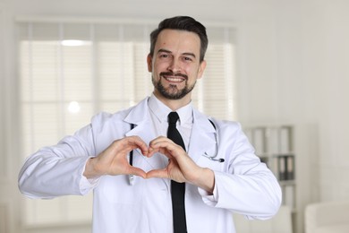 Photo of Smiling cardiologist making heart with hands in clinic