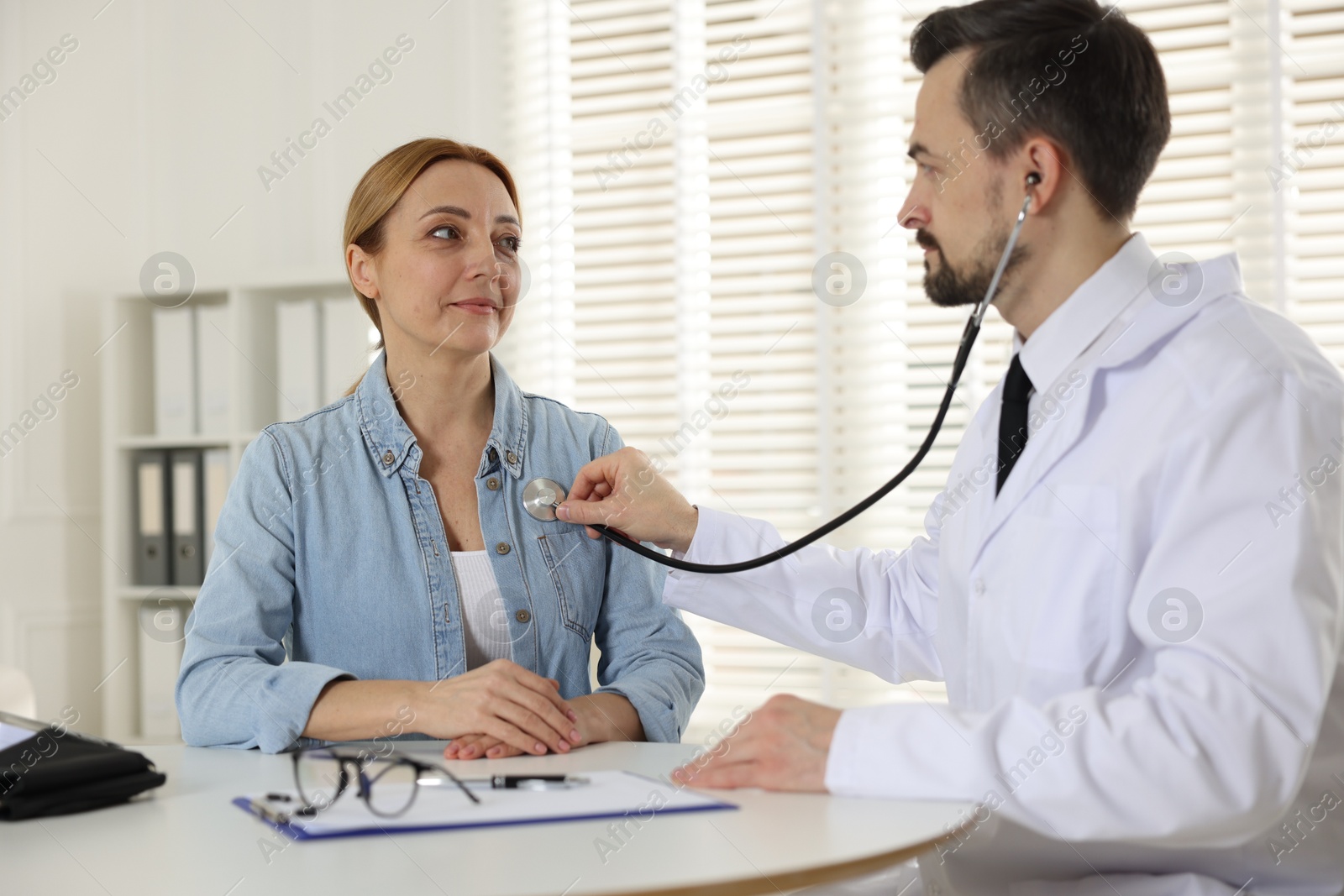 Photo of Cardiologist with stethoscope listening patient's heartbeat at desk in clinic