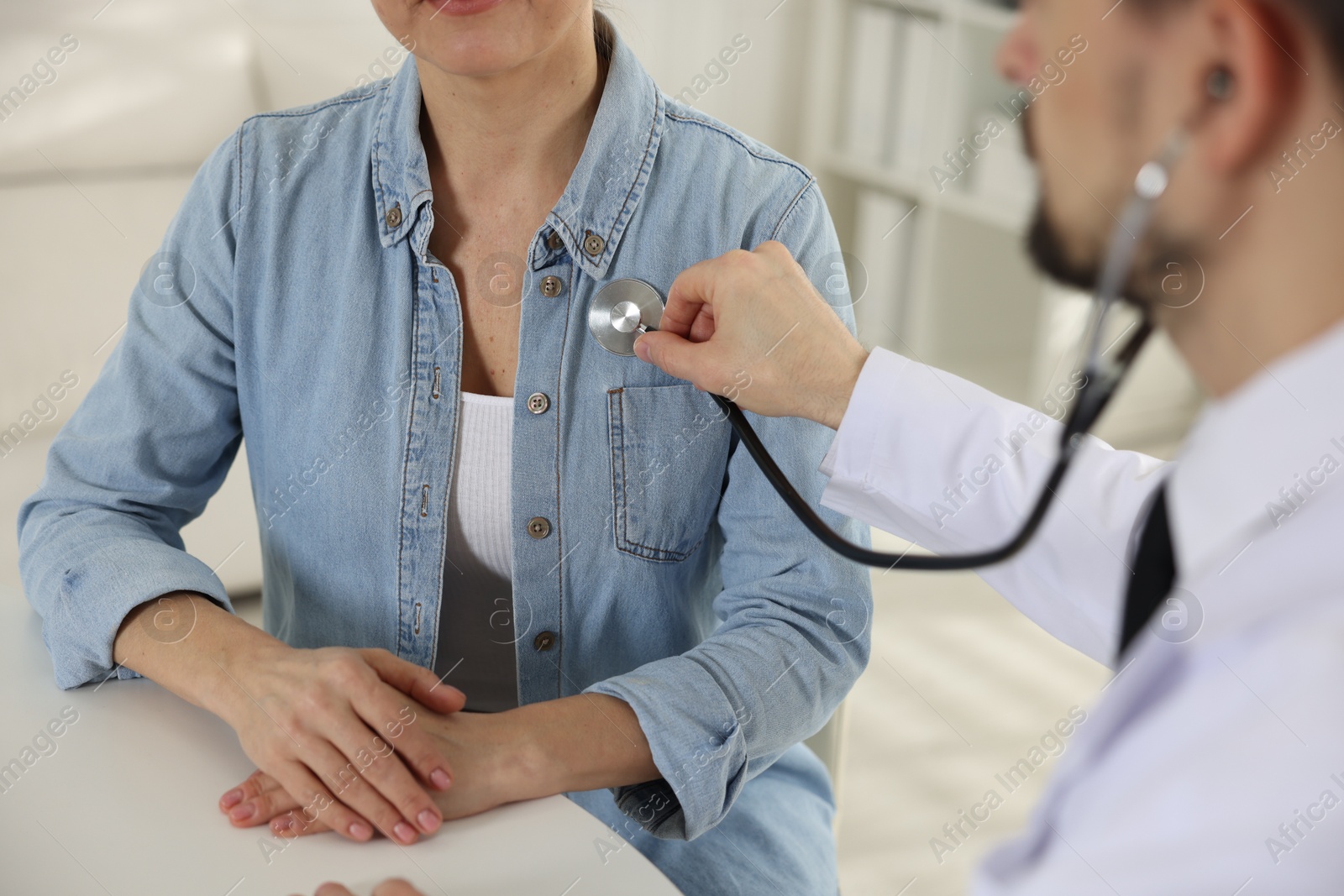 Photo of Cardiologist with stethoscope listening patient's heartbeat at desk in clinic, closeup