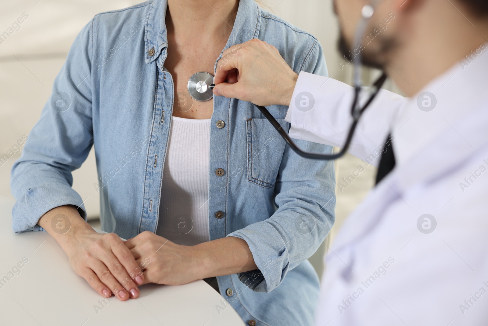 Photo of Cardiologist with stethoscope listening patient's heartbeat at desk in clinic, closeup