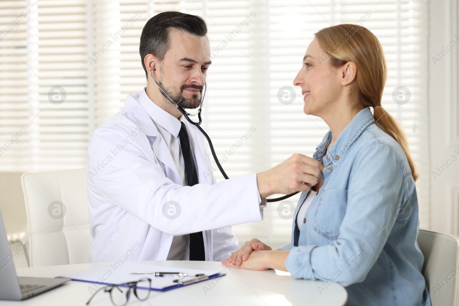 Photo of Cardiologist with stethoscope listening patient's heartbeat at desk in clinic