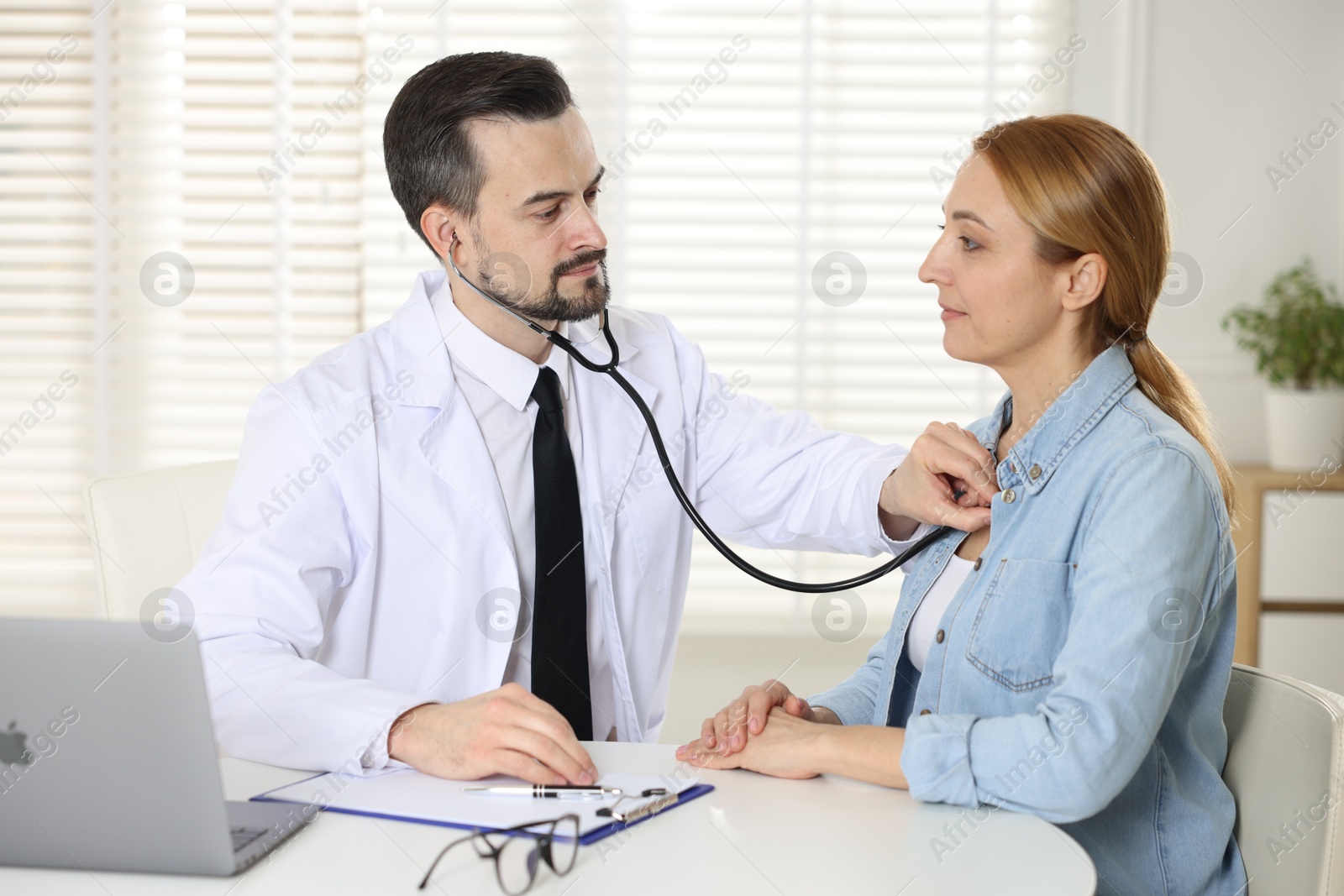 Photo of Cardiologist with stethoscope listening patient's heartbeat at desk in clinic