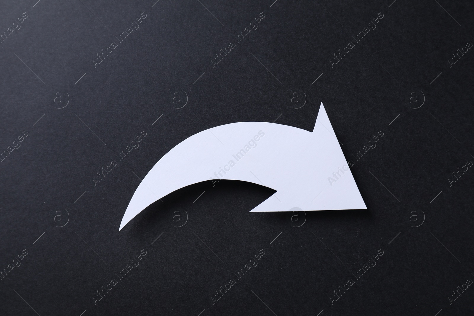 Photo of One white paper arrow on black background, top view