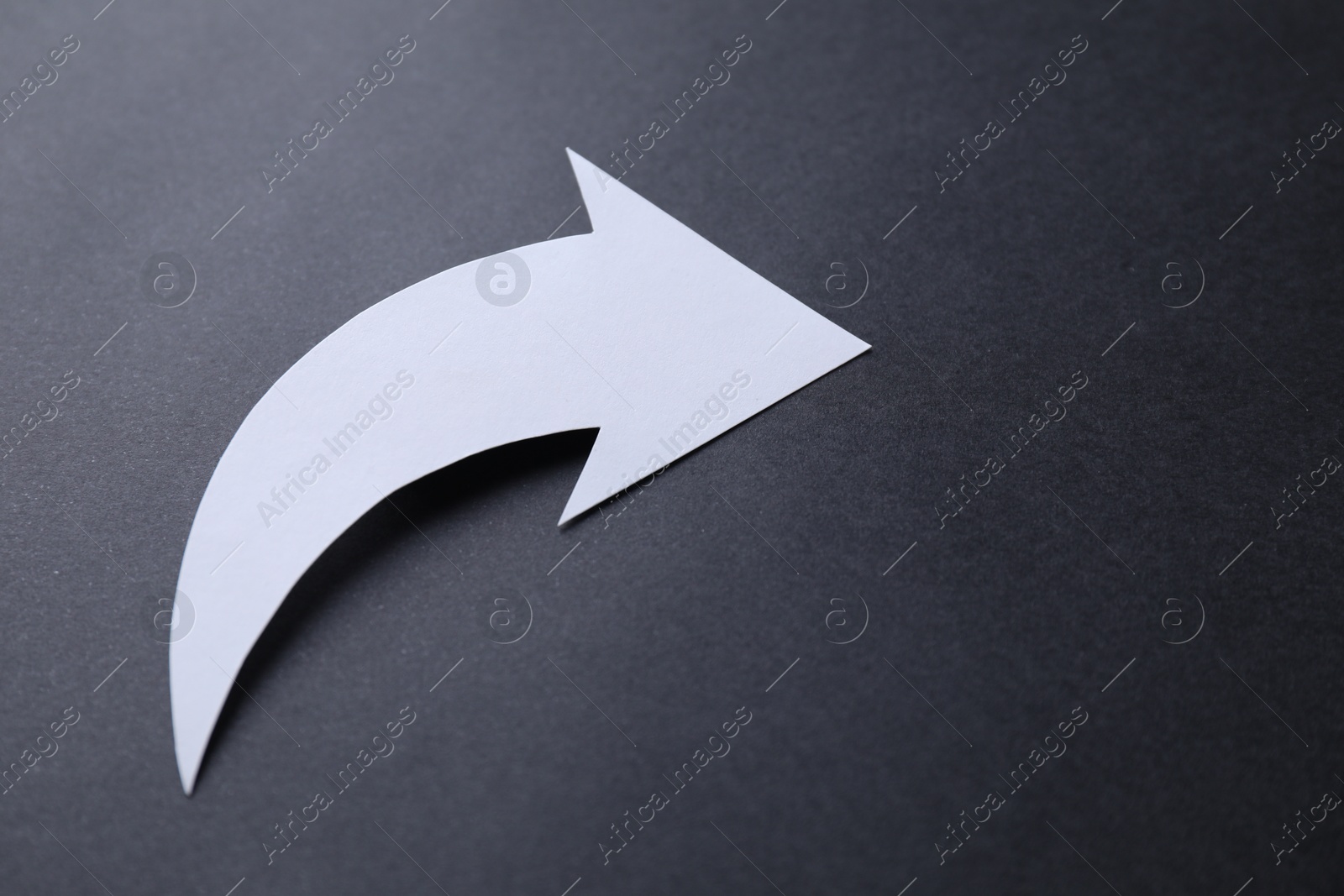 Photo of One white paper arrow on black background, closeup