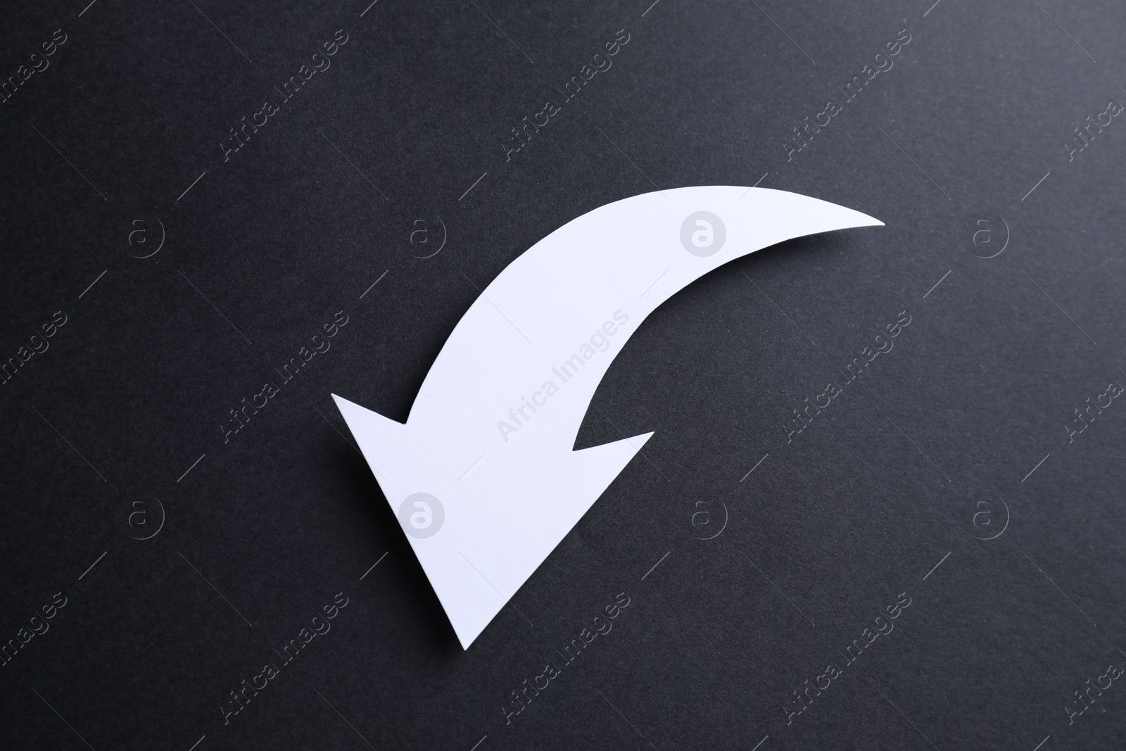 Photo of One white paper arrow on black background, top view