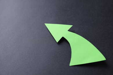 Photo of One green paper arrow on black background, closeup. Space for text