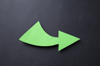 Photo of One green paper arrow on black background, top view