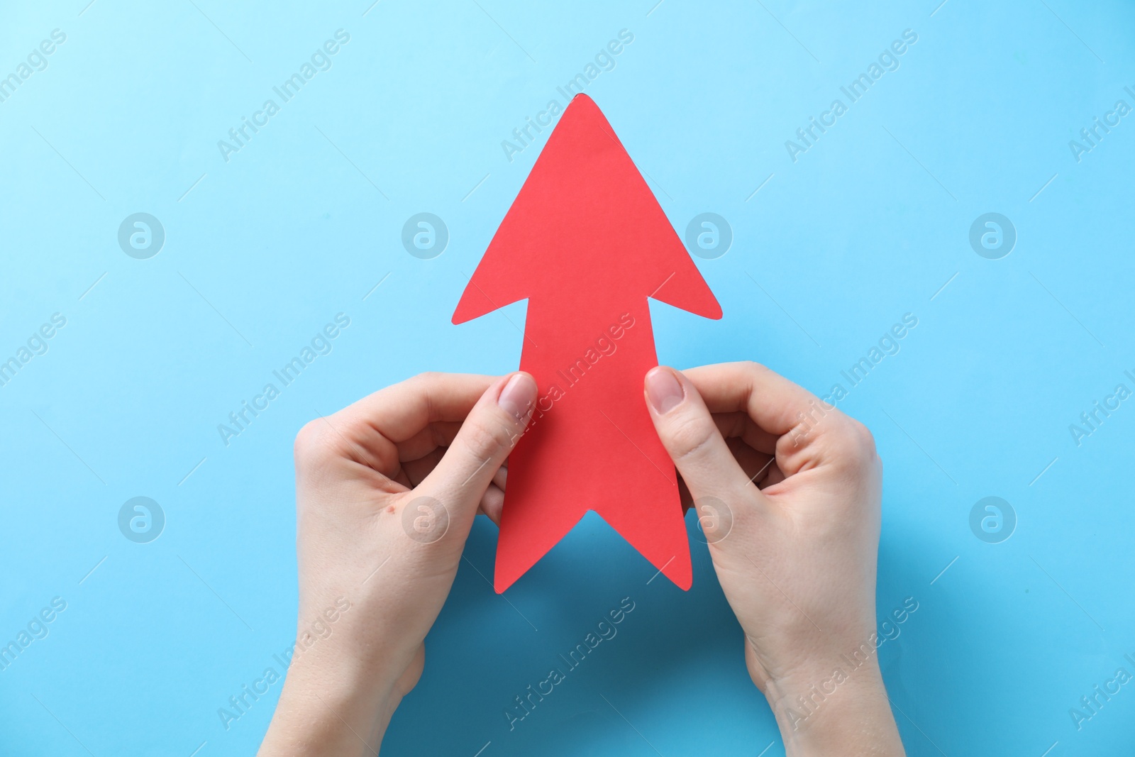 Photo of Woman with paper arrow on light blue background, top view