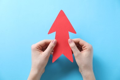 Photo of Woman with paper arrow on light blue background, top view