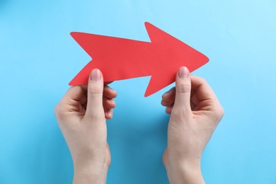 Photo of Woman with paper arrow on light blue background, top view