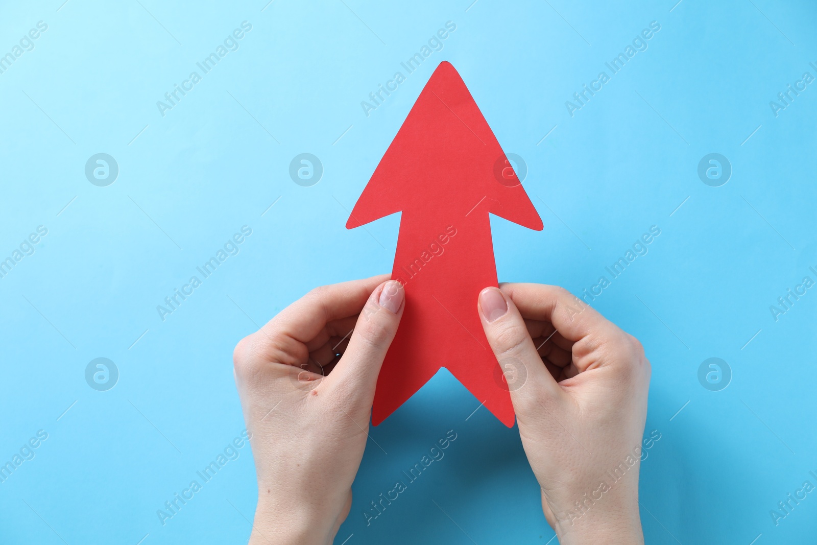 Photo of Woman with paper arrow on light blue background, top view