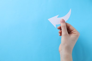 Photo of Woman with paper arrow on light blue background, top view. Space for text