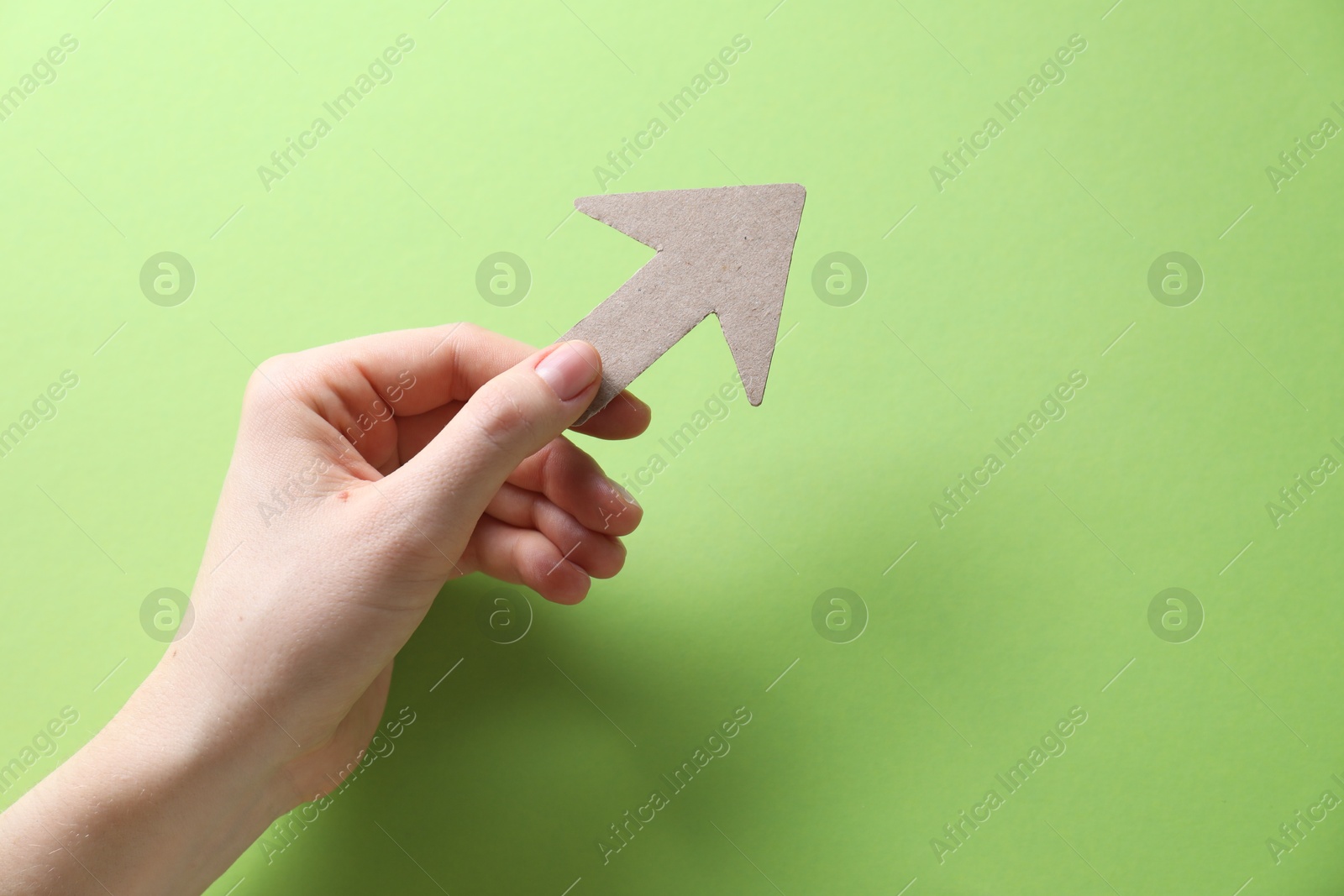 Photo of Woman with paper arrow on light green background, top view. Space for text