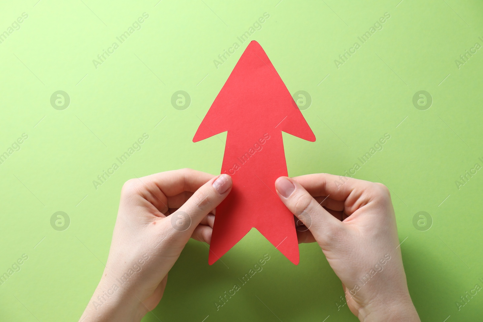 Photo of Woman with paper arrow on light green background, top view