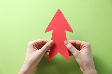 Photo of Woman with paper arrow on light green background, top view