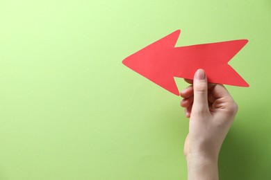 Photo of Woman with paper arrow on light green background, top view. Space for text