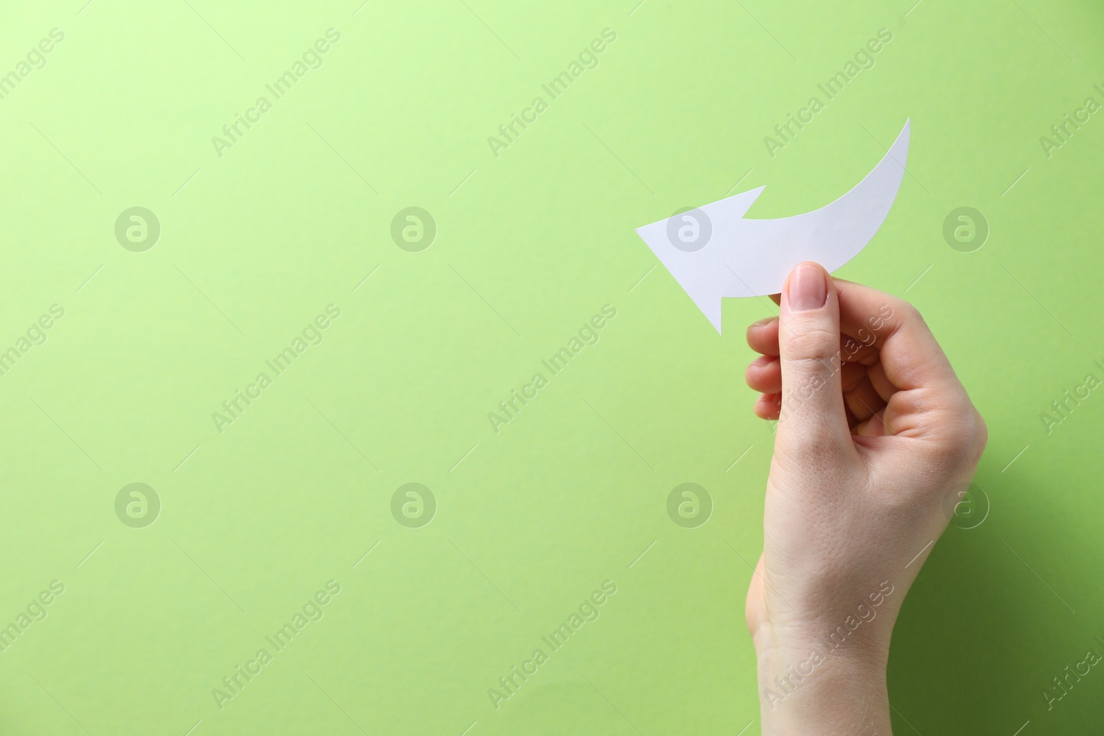 Photo of Woman with paper arrow on light green background, top view. Space for text