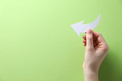 Photo of Woman with paper arrow on light green background, top view. Space for text