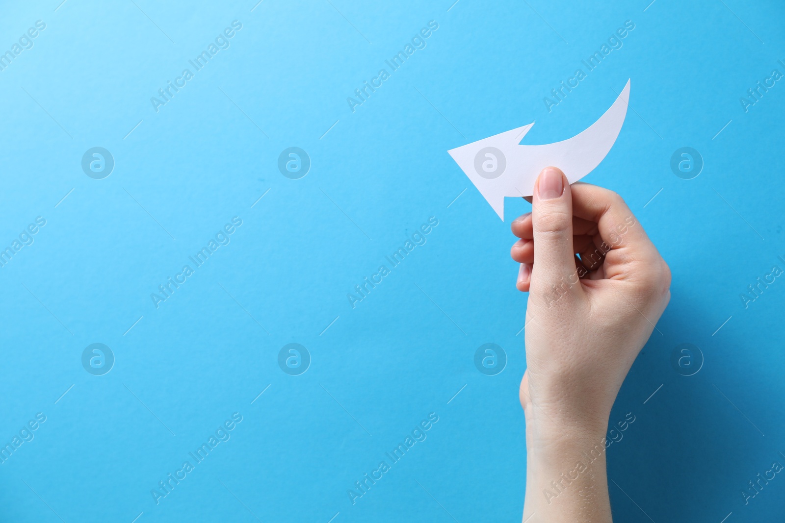 Photo of Woman with paper arrow on light blue background, top view. Space for text