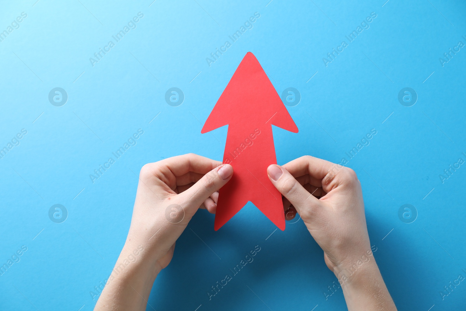 Photo of Woman with paper arrow on light blue background, top view