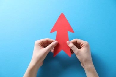 Photo of Woman with paper arrow on light blue background, top view