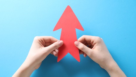 Photo of Woman with paper arrow on light blue background, top view